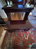 Photo of the dark wood two-step bed stool on a patterned rug with curved support and top rail
