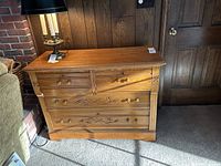 Full view of the wooden chest of drawers showing its size, drawer configuration, wood grain, and surrounding environment.