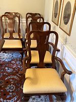 Rear and front view of 6 dining chairs arranged in a row, showing upholstery and carved wood backs.