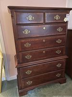 Front view of the tall wooden dresser showing its seven drawers, brass handles, and some surface wear.