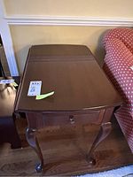 Wooden drop leaf table shown with leaf extended on one side and drawer closed.