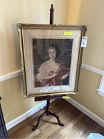 Framed portrait of a woman on a wooden easel stand, showing full view of the item and floor setting