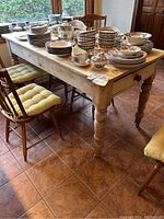 Full view of pine farmhouse table topped with dishware and surrounded by chairs.