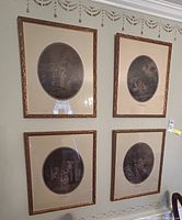 Set of four framed vintage art prints on wall, each containing an oval image with ornate gold-colored frames. Prints depict classical people and outdoor scenes.