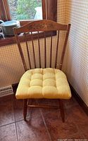 Full view of a wooden Hitchcock chair with yellow cushion, showing the spindle back and floral stenciling on the top rail