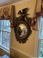 Full view of the decorative wall mirror with eagle figure mounted on the wall between two windows.