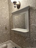 White bathroom wall mirror mounted above bathroom sink, showing the shelf and three peg hooks underneath the shelf.