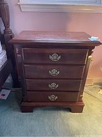 Front view of wooden nightstand showing four drawers with decorative metal handles, classical design legs and moldings.