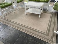Full view of rectangular beige outdoor rug under white wicker outdoor furniture with green cushions.