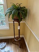 Wooden plant stand with woven basket and artificial fern in corner near window.