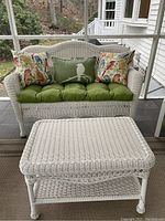 View of white plastic wicker two-seater bench with green seat cushion and three decorative pillows along with matching coffee table, showing overall condition and style.