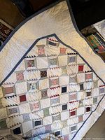 Full view of quilt showing overall patchwork design with spools of thread pattern and triangular blocks. Muted blue border frames the quilt.