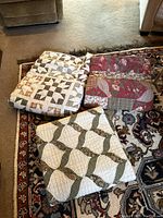 Three folded quilts on floor showing their patchwork designs, stacked together on a rug.