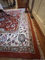 Rug corner showing red field and ivory floral border with fringe