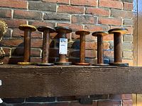 Seven vintage wooden spools arranged on a wooden beam against a brick wall, showing variety in size and color of painted spool ends.