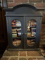 Full view of dark wooden display case with two glass doors, showing entire collection of miniature books inside.