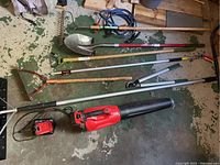 Top view of all the tools laid on the ground including long-handled rake, shovel, tree clipper, snow shovels, blower and batteries.