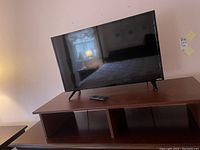 Full view of the Vizio TV on the wood riser with remote control visible on top of the riser.