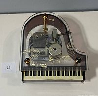 Top view of transparent mini grand piano music box showing internal mechanical music components and gold-tone music notes decoration.