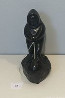 Front view of black fishing figurine showing person in hooded attire holding fishing line with fish on rocky textured base.