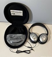 Bose QuietComfort 15 wired headphones displayed with carrying case and instruction manual inside the case.