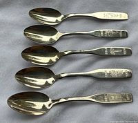 Top view of five shiny metal commemorative spoons arranged side by side, showing bowl and part of handle with year engravings.