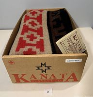 Kanata Blanket folded inside its original branded box with tag visible, showing the label 'Kanata Blanket Co.' and 'C. Road Red' color designation.