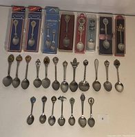 Full display of 27 vintage collectors spoons including packaged and loose items with varied ornate handle designs.