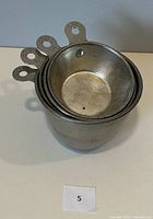 Stacked view of four metal measuring cups nested inside each other, showing handles with stamped measurements.