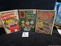 Photo showing three vintage comic books: Dennis the Menace Giant Christmas Issue, Dell Giant Walt Disney Huey, Dewey and Louie Back to School, and Dennis the Menace Hawaii.