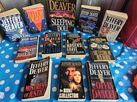 Photo showing 12 Jeffery Deaver paperback novels arranged on blue polka-dot fabric.