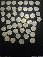 Top-down view of 48 American state quarters arranged on a black surface showing front and back designs with various state symbols and landmarks.