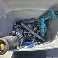 Top view of bin containing Makita electric drill, rotary tool, reciprocating saw, cords and hand tools