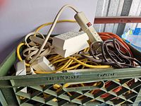Pile of multiple yellow, orange, and brown electrical cords and power bars inside green plastic crate.