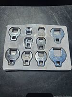 Photo of 11 crows feet open ended wrenches arranged in a white foam holder, one slot is empty indicating a missing wrench.