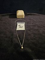 Front view of the cultured pearl necklace displayed flat with a jewelry box in the background on black fabric.