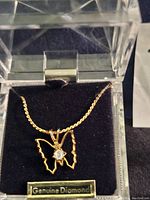 Close-up of the butterfly-shaped pendant necklace with small diamond at the center inside original display case with 'Genuine Diamond' label.