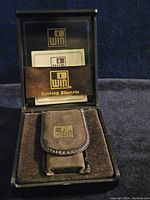 Closed molded black box with dark brown velvet lining and a brown velvety carrying pouch inside, branded 'win Battery Electric'