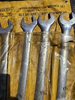 Four large combination wrenches in a yellow fabric pouch with clear plastic sleeves, showing size markings and signs of use.