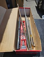 Long cardboard box containing a red plastic socket holder with numerous sockets and several long metal extensions including a Snap-on 1/2" impact extension and other extension bars.