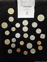 Top-down view of all approximately 25 coins arranged on a black surface with a note describing the lot contents including American dimes and nickels and foreign coins.