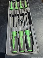 Seven green-handled Snap-on Torx screwdrivers in gray foam tray, three positioned at bottom, four at top with one loose bit in center