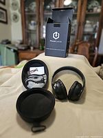 Black PowerLocus wireless headphones displayed next to open black carrying case containing cables and documentation, with box behind them.