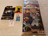 Photo of the full Batman lot showing all items arranged on a carpeted floor: Hot Wheels toy, vintage keychain, trading cards, and three comic books.
