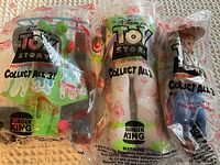 Photo of three sealed Burger King Toy Story toys in original plastic bags showing Buzz Lightyear, Woody, and a car with packaging labels and logos visible.
