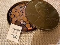 Metal container with Abraham Lincoln embossed lid, filled with wheat pennies and some extra coins