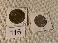 Photo of two coins: 1978 Eisenhower dollar labeled '78 BU' and 1967 Kennedy half dollar labeled '1967' in cardboard holders on a textured fabric background.