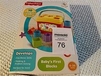 New Fisher Price Baby's First Blocks box showing front with 10 colorful blocks, container and lid with yellow top and red base. Box has a dented top corner.