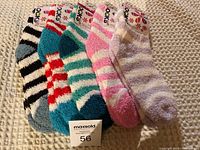 Five pairs of fuzzy socks in striped patterns arranged side by side on a knitted beige surface.