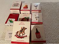 Photo showing 9 Hallmark Keepsake ornament boxes placed on a light carpet. Ornaments include a rocking horse, beer bottle, ducks, a dog, and other holiday designs.